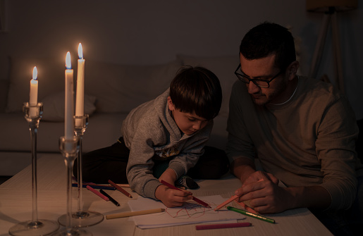 Child and Father Painting By Candlelight During A Power Outage