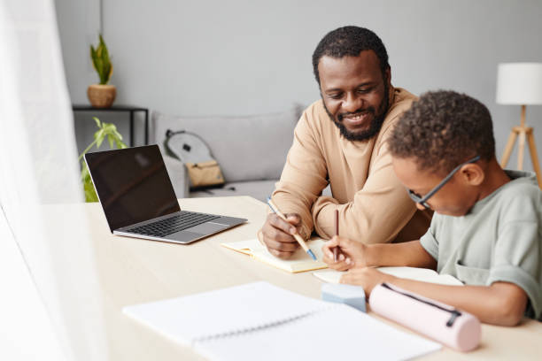 African American Boy Studying with Father at Home Portrait of smiling African-American father helping son with homework while studying at home, copy space homework table stock pictures, royalty-free photos & images