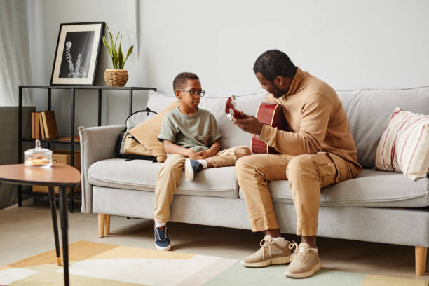 Father Teaching Son Guitar Lesson Full length portrait of African-American father teaching son to play guitar and musical instruments, copy space father and son guitar stock pictures, royalty-free photos & images