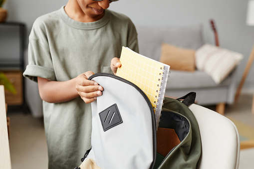 Close up of young African-American boy packing backpack at home, copy space