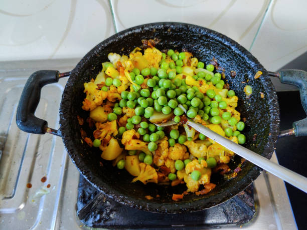 Stock photo of delicious, hot Indian mix vegetable curry, mix veg containing green peace, onion, tomato, potato cauliflower and curry leaves with Indian spice cooking in the iron cauldron in kitchen. stock photo