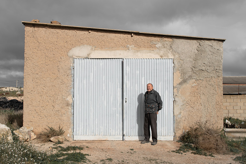 Old farmer is posing in front of his garage with a smile.