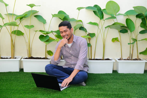 Adult Asian man smiling happy when working in the outdoor park using his laptop computer Adult Asian man smiling happy when working in the outdoor park using his laptop computer kantor stock pictures, royalty-free photos & images