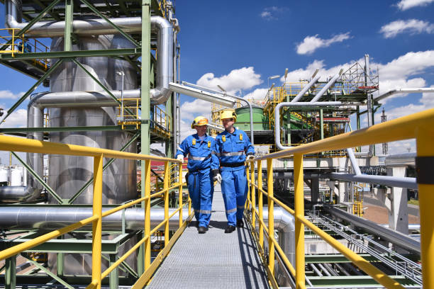 usine de l’industrie chimique - travailleurs en vêtements de travail dans une raffinerie avec des tuyaux et des machines - usine pétrochimique photos et images de collection