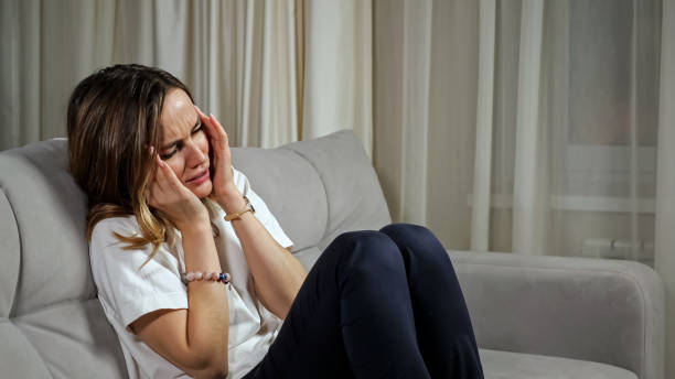 istock Woman handles headache sitting on sofa in living room 1366558986