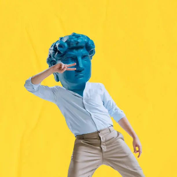 Photo of Young man headed by blue statue head dancing isolated on yellow background. Contemporary colorful and conceptual bright art collage