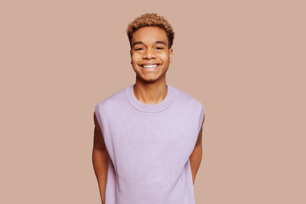 Happy young afro black latin american man smiling posing at studio Glad young afro latin american black handsome man feels great, wears in purple top, broadly smiles and looks in camera stands over beige background. alternative pose stock pictures, royalty-free photos & images