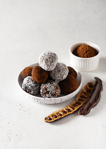Carob energy balls with nuts, dates and coconut, vegan and vegetarian sweet food, white background, copy space, vertical