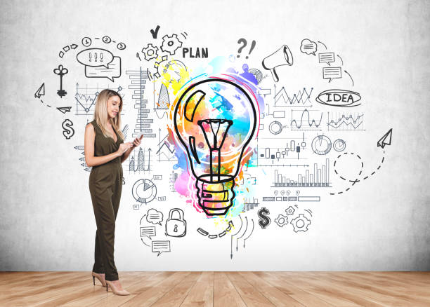 istock Businesswoman using smartphone, colourful lightbulb sketch on grey wall 1366565817