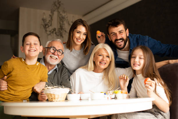 uma família de três gerações na sala de jantar, na mesa. eles estão aproveitando a preparação para as férias de páscoa. - two generation family holiday vacations easter egg - fotografias e filmes do acervo