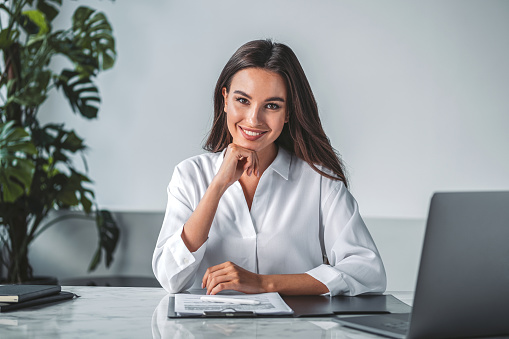 Office woman happy look in white office room, laptop and clipboard with papers on the table. Desk with notebook and technology. Concept of business secretary