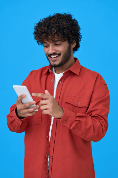 istock Happy indian young man using cell phone isolated on blue background. 1366571467
