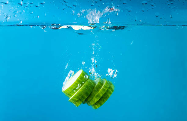 istock Falling of fresh cucumber slices into water against blue background 1366571663