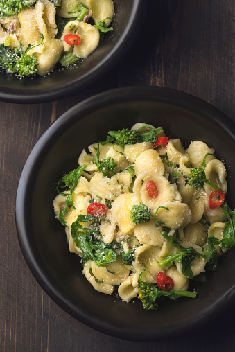 Italian pasta Orecchiette with turnip leaves (cima di rapa) and tops with garlic, hot pepper, grated bread on a dark wooden background. Recipes of southern Italy, Puglia. Poor cuisine or cuisine of simple ingredients, close up