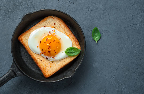 istock Fried eggs with pepper and basil on toast in a frying pan on a graphite background 1366574199