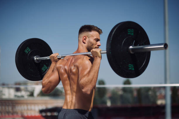 Sportsman doing exercise with barbell outdoors