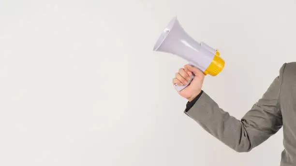Photo of The man's hand is holding a megaphone and wears a grey suit on white background.