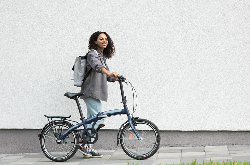 Smiling african-american woman holding a bike looking up outdoor. Travel, people and active lifestyle concept