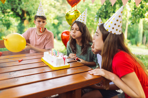Group of children enjoying and having a lot of fun while celebrating on birthday party in backyard. They are happy and playful, blowing candles on cake