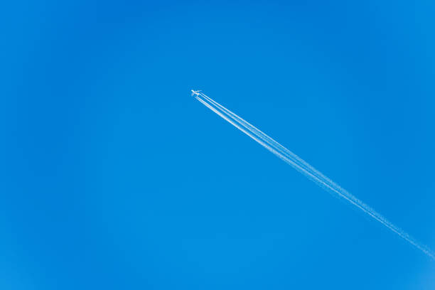 A white Airliner with contrails flying in a clear blue sky, seen directly below, photography.
