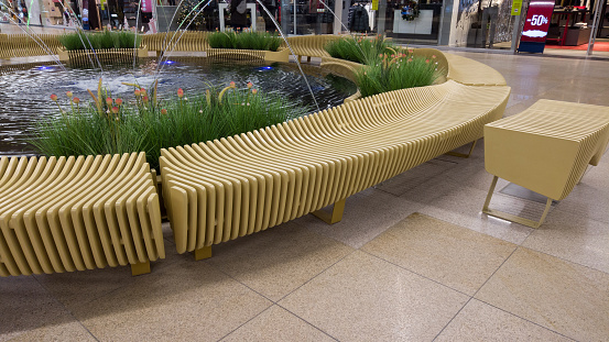 Wooden bench in the shopping mall. Recreation area in the shopping center with wooden benches and artificial pond with fountains.