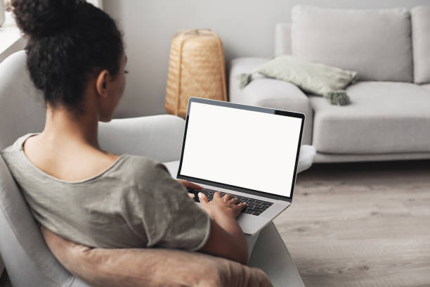 Woman using laptop computer on sofa, white blank empty screen mock-up Young african american woman working at home, girl studying online. Entrepreneur, business, web site add, freelance, business, studying, social distancing, distance learning, work from home, modern lifestyle, laptop mock up concept using laptop home stock pictures, royalty-free photos & images