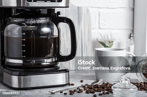 istock A black drip electric coffee machine with a glass teapot brews a morning drink. Household appliances, a white cup and a jar of beans on the kitchen table on the countertop at home 1366583927