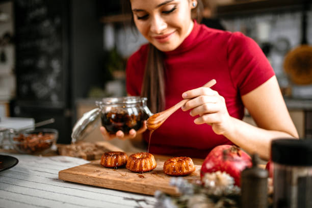 Woman spicing doughnuts with honey using wooden spoon.