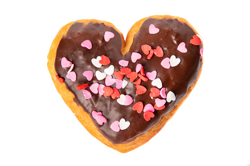A heart shaped donut with heart sprinkles on it's chocolate icing isolated on a white background.