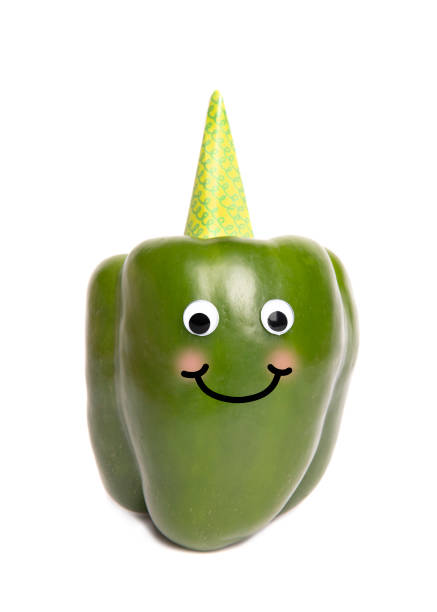 A green bell pepper in a party hat with googly eyes and a big smile.