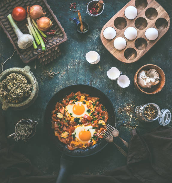 Tasty fried eggs in tomato sauce in black pan with fork on rustic background. Top view. Shakshuka breakfast. Ingredients. Cooking. Healthy food eating