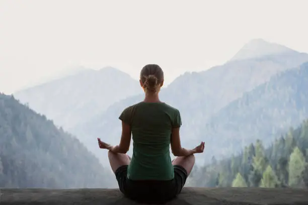 Fit girl meditating, doing relaxation exercises with mountains at background. Meditation, healthy lifestyle, self care, yoga, leisure concept
