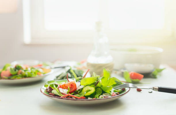 Plate with fresh green salad and fork on table at sunny kitchen background. stock photo