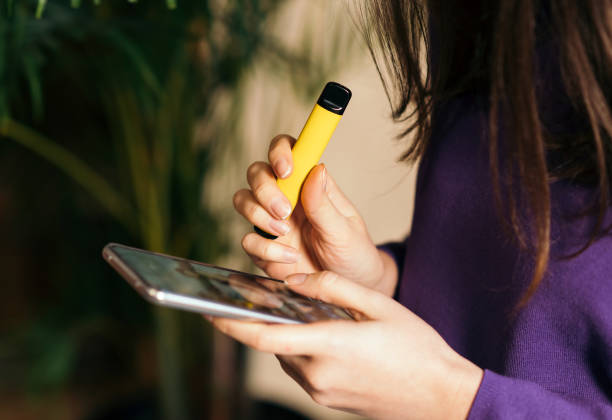 บุหรี่อิเล็กทรอนิกส์สีเหลืองในมือของผู้หญิง การสื่อสารออนไลน์ที่ทันสมัย - disposable ภาพสต็อก ภาพถ่ายและรูปภาพปลอดค่าลิขสิทธิ์