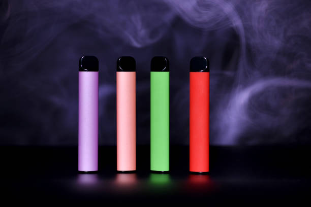 色の煙と黒の背景にカラフルな使い捨て電子タバコのセット。現代の喫煙、空洞化、ニコチンの概念。 - 電子タバコ ストックフォトと画像