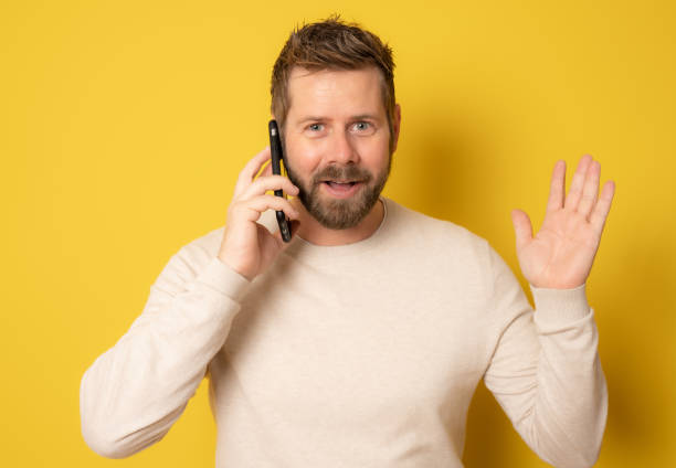istock Young man in casual sweater talking on smartphone looking at camera with surprised face isolated over yellow background. 1366588012