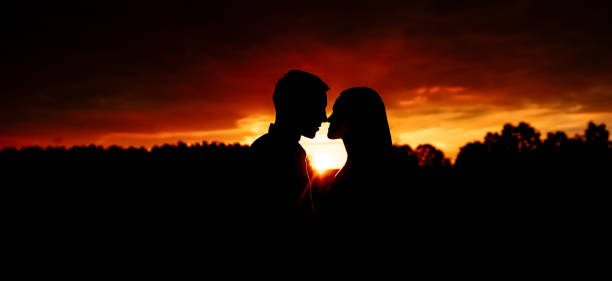 silueta de una joven pareja enamorada cara a cara contra el fondo del cielo naranja durante la puesta de sol. - heterosexual couple love romance couple fotografías e imágenes de stock