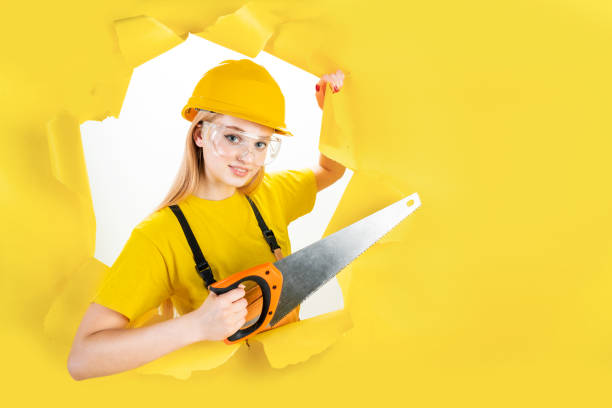 istock Woman in protective helmet is holding manual saw 1366588578