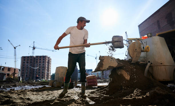 молодой человек, работающий с лопатой и бетономешалкой. - construction safety mid adult men road construction стоковые фото и изображения