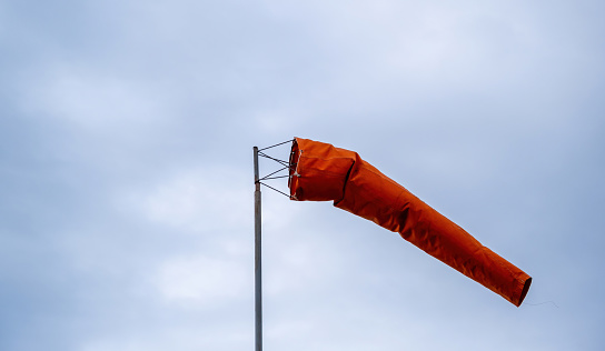 Windsock blowing on cloudy sky. Red cone, wind speed and direction indicator. Windy day at the airport.