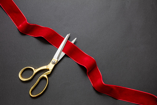 Inaugural invitation, business launch concept, Grand opening, ribbon cut, Gold scissors cutting red velvet ribbon on black background, copy space