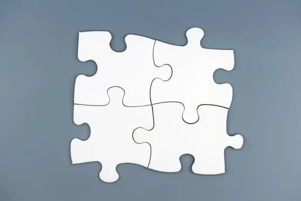 Photo of Four white puzzle pieces on gray background