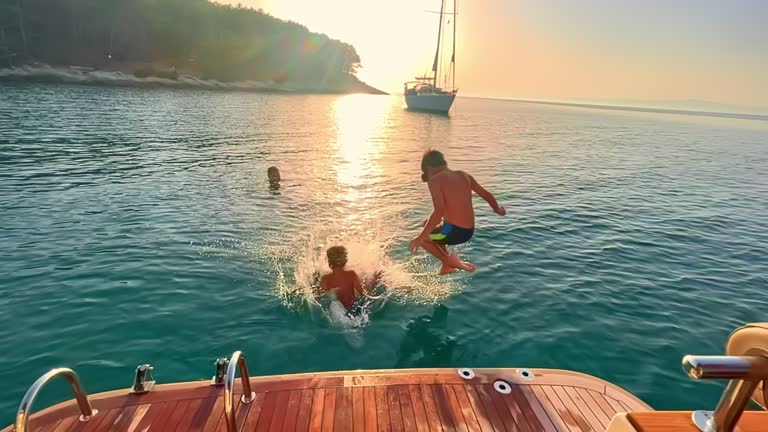 SLO MO Two young brothers jumping off the boat into the sea at sunset