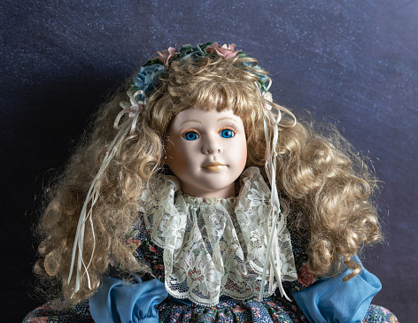 Amazing realistic vintage toy with blue eyes.The doll dressed in a blue dress and has a blond hair. Selective focus. Porcelain.