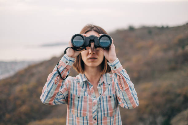 Beautiful woman with binoculars looks into the camera on background of the mountain.