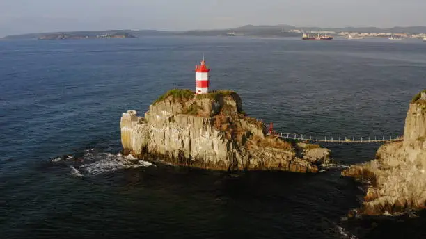 Drone view of the picturesque old Basargin lighthouse on the coast of the Sea of Japan. Russia, Vladivostok. Orange dawn. Flocks of seagulls fly over the coast.