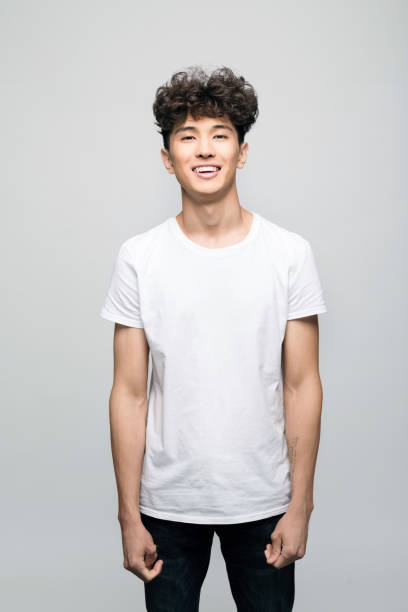 Friendly young man in white t-shirt Portrait of cheerful young man wearing white t-shirt. Male student smiling at camera. Studio shot, grey background. teenager boy haircuts stock pictures, royalty-free photos & images