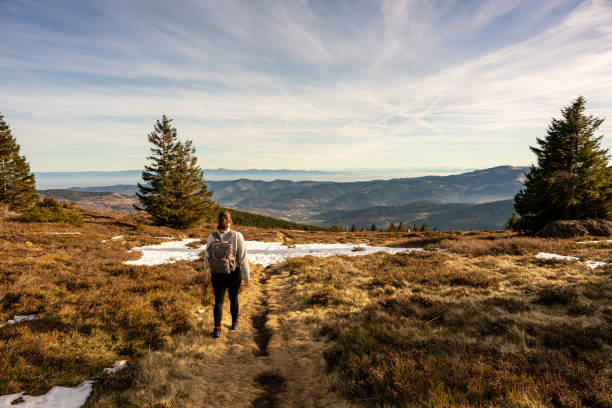 Beautiful autumn landscape of mountain top area with young woman walking toward the horizon at sunset