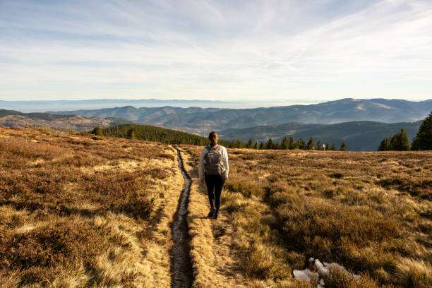 Beautiful autumn landscape of mountain top area with young woman walking toward the horizon at sunset