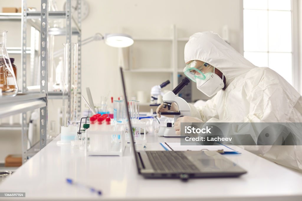 Unrecognizable scientist pharmacologist in protective uniform at laboratory Unrecognizable scientist pharmacologist in disposable protective uniform using microscope working on medicine, biotechnology research in advanced pharma lab. Medical development laboratory 20-24 Years Stock Photo